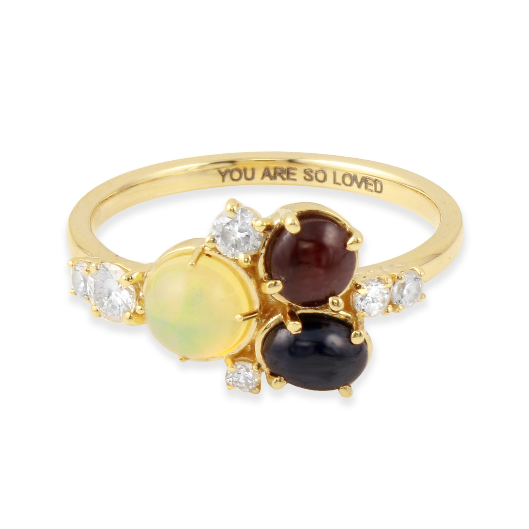 a close up of a 14k gold ring with a ruby, opal, blue sapphire and white diamonds and the engraving you are so loved inside the band