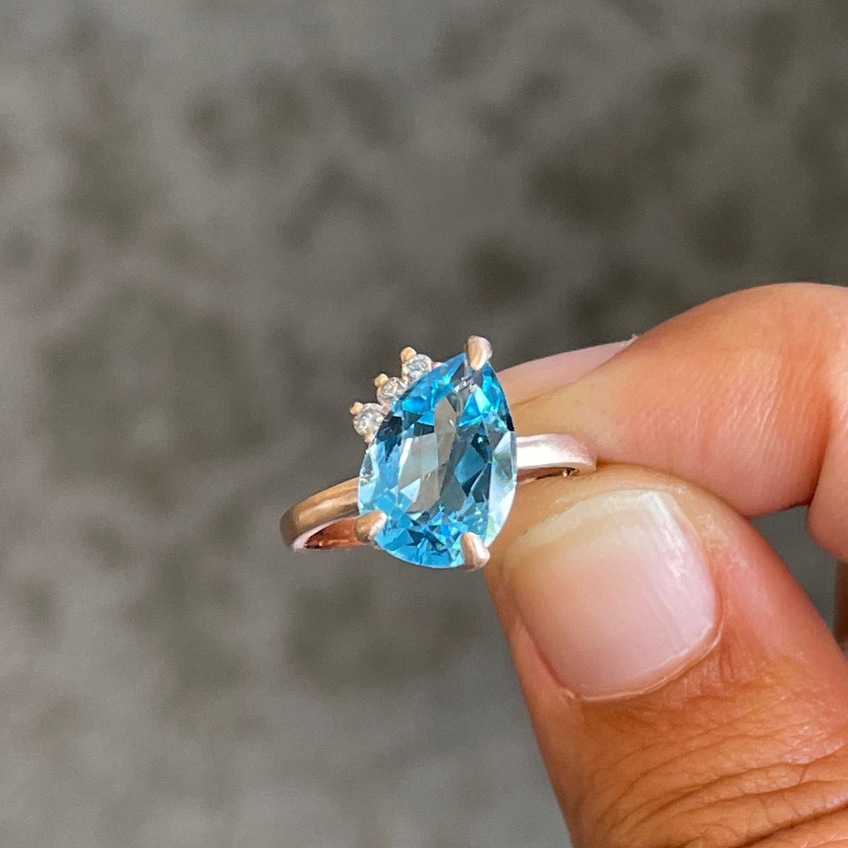 a close up of a hand holding a rose gold ring with a bear shaped blue topaz stone and a crown of three diamonds